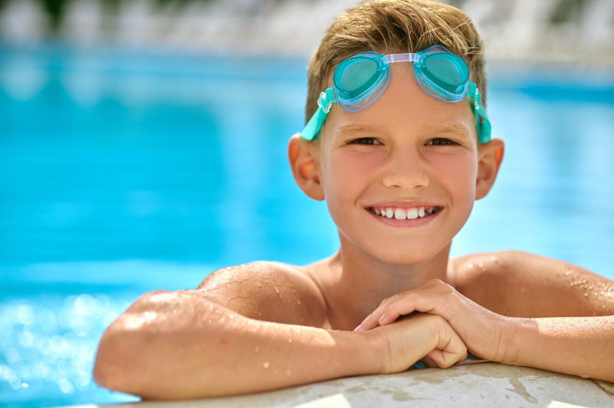 boy with goggles smiling at camera in pool